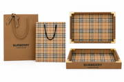 This gift packaging set featuring a brown paper shopping bag, a matching plaid shopping bag, and two plaid-lined gift boxes with gold-tone corner protectors, all on a white background.